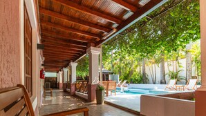 Un espacio al aire libre cubierto con piscina, mobiliario de madera y un banco.