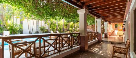 A covered outdoor area with a pool, wooden deck, and seating.