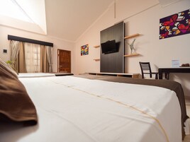 Una habitación de hotel con una cama grande, un escritorio, un televisor y una ventana con cortinas.