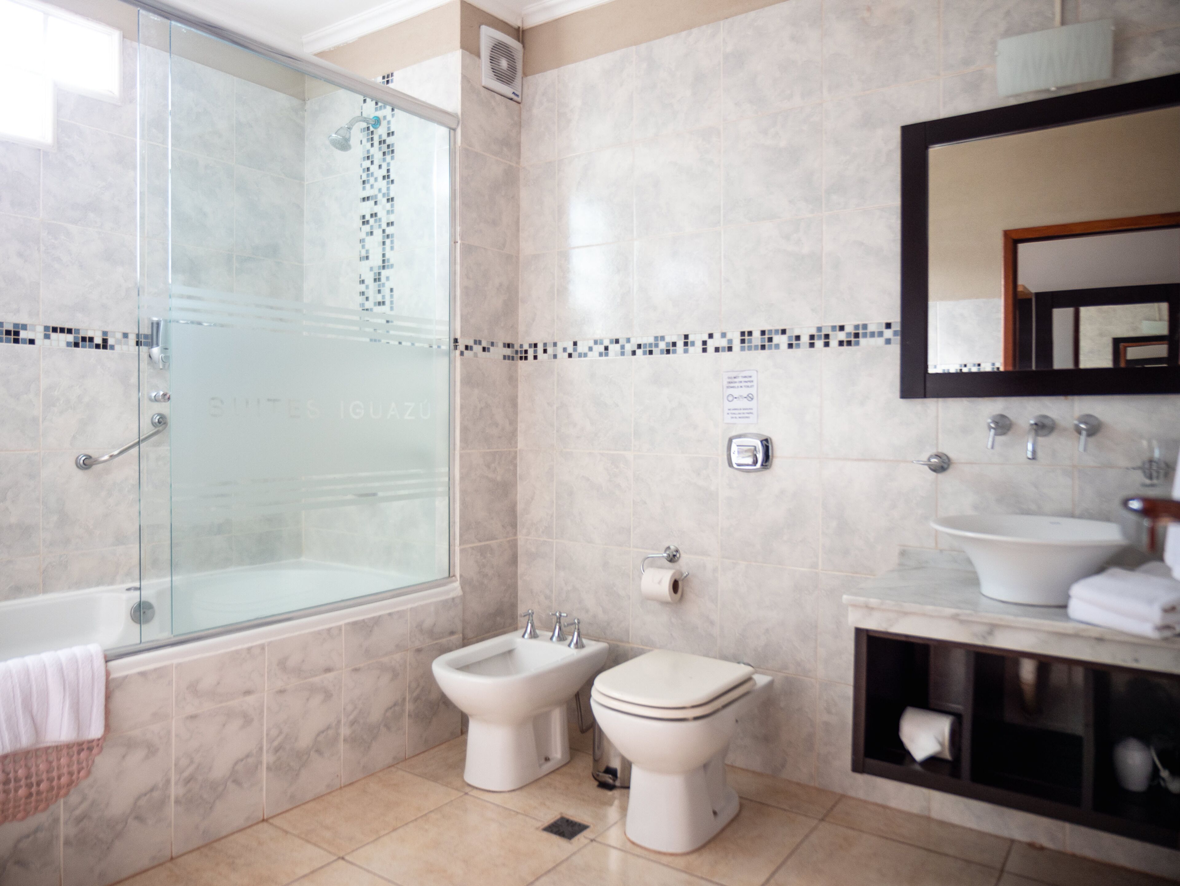 A bathroom with a glass-enclosed shower, a bidet, a toilet, a sink, and a mirror.