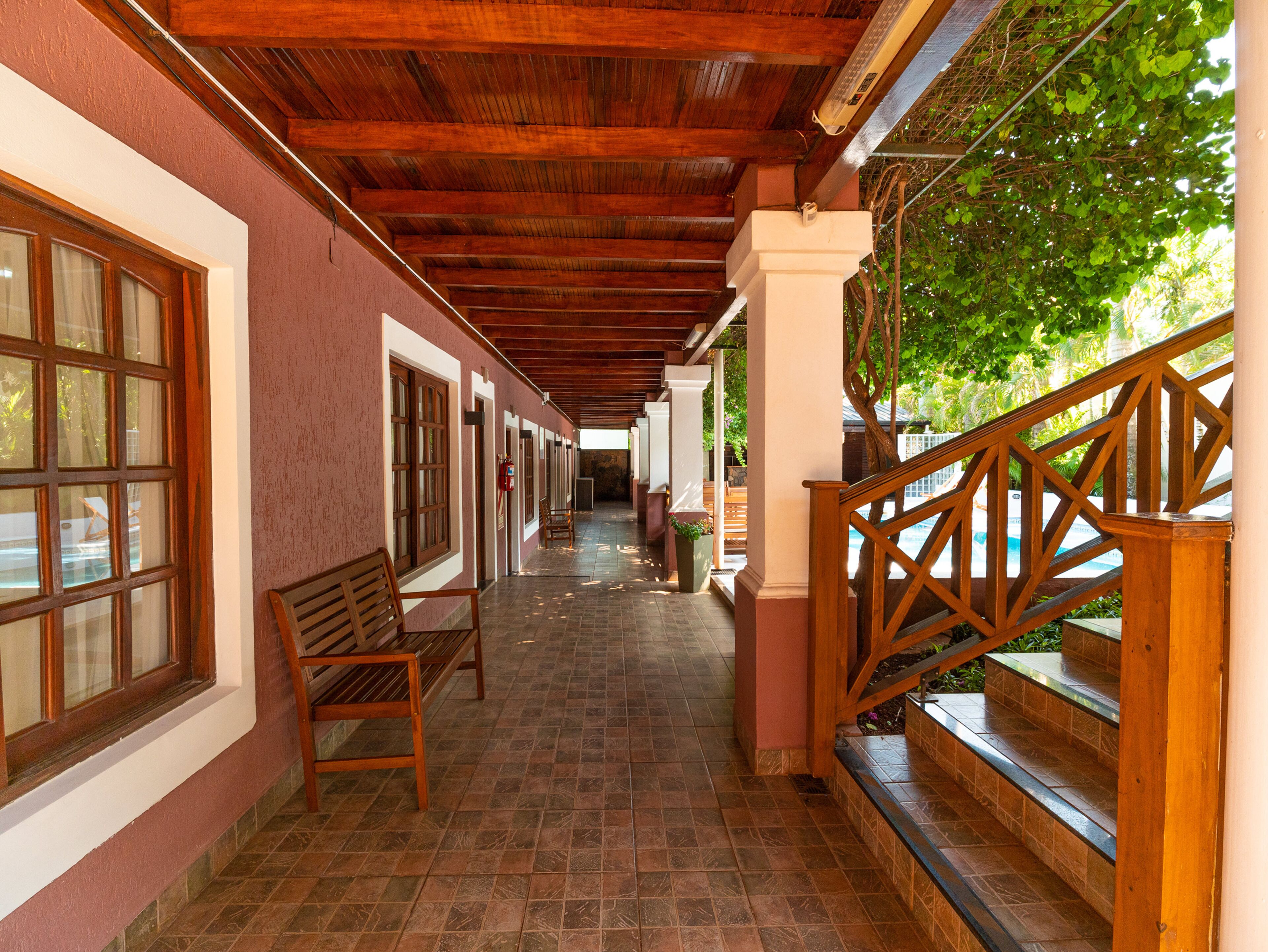 A covered corridor with wooden benches and a staircase leading to a pool area.