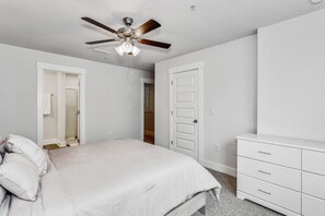A bedroom with a bed, a ceiling fan, a white dresser, and a door leading to a closet. - LUXURY TOWNHOME NEAR DOWNTOWN AND PENSACOLA BEACH (Pensacola)
