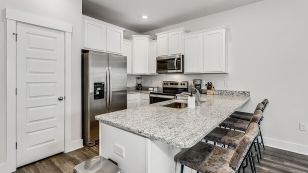 A modern kitchen with white cabinets, stainless steel appliances, a granite countertop, and bar stools. - LUXURY TOWNHOME NEAR DOWNTOWN AND PENSACOLA BEACH (Pensacola)