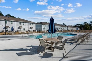 A poolside area with lounge chairs and umbrellas, a pool, and a row of white buildings in the background. - LUXURY TOWNHOME NEAR DOWNTOWN AND PENSACOLA BEACH (Pensacola)
