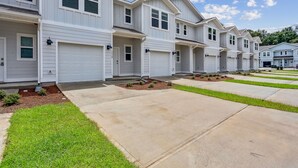A row of modern townhouses with white siding, garage doors, and small front yards with grass and mulch. - LUXURY TOWNHOME NEAR DOWNTOWN AND PENSACOLA BEACH (Pensacola)