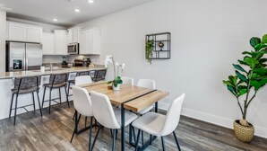 A modern kitchen with white cabinets, a wooden dining table, and a potted plant. - LUXURY TOWNHOME NEAR DOWNTOWN AND PENSACOLA BEACH (Pensacola)