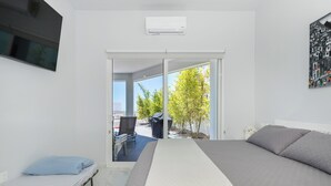 A bedroom with a bed, a small table, a chair, and a sliding glass door leading to an outdoor area with a chair and a table. - Beach Front House - EV charging included (Son.)