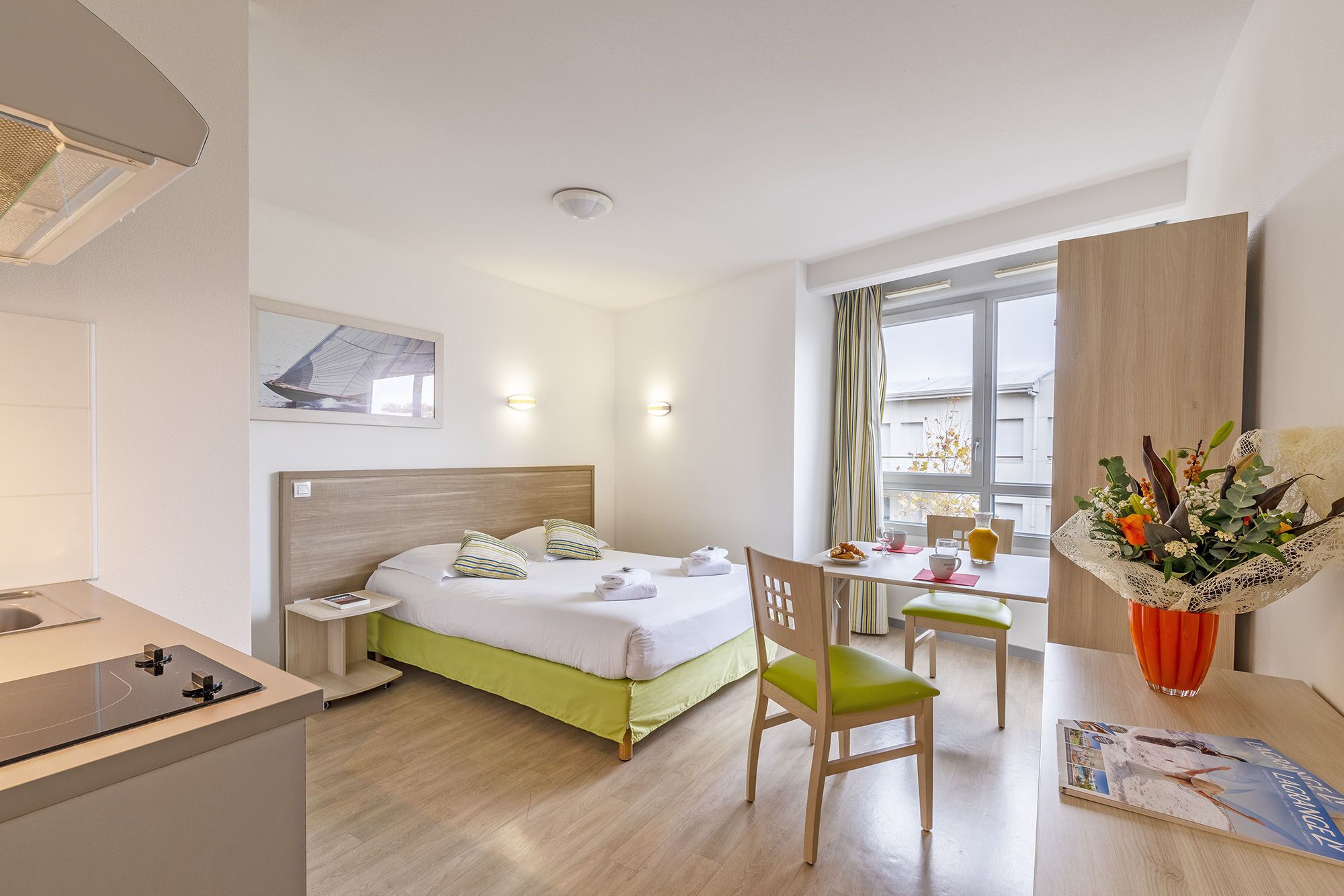 Una habitación de hotel con cama, escritorio, silla, mesita y ventana con cortinas.