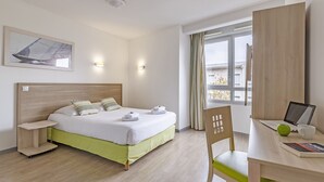 Habitación de hotel con cama, mesita de noche, silla, escritorio, computadora y ventana con cortinas.