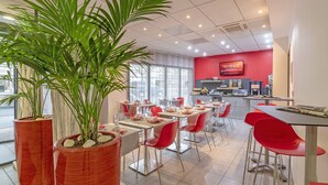 Un interior de restaurante moderno con decoración roja y blanca, varias mesas y plantas en macetas.