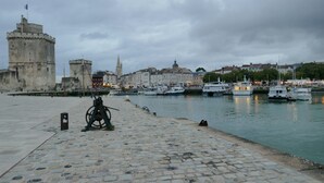 Un paseo marítimo con una torre histórica, barcos amarrados y un camino adoquinado.
