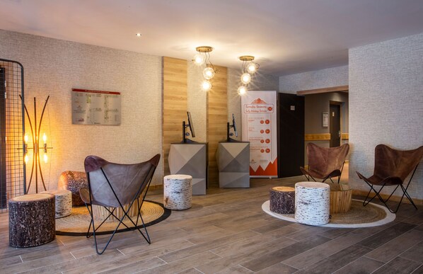 A modern lobby with a wooden floor, leather chairs, and a central table. There are informational posters on the walls and a map.