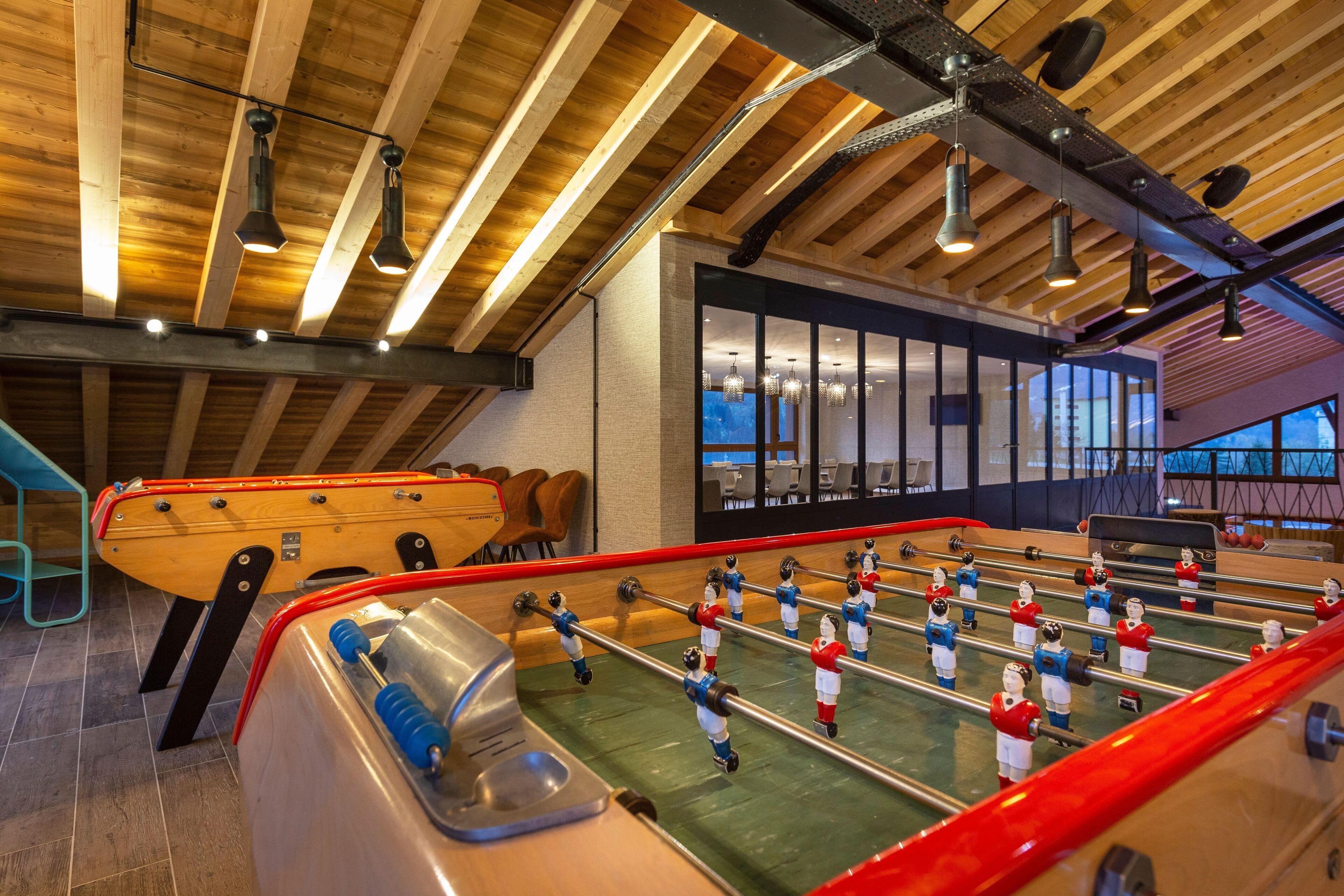 Une table de baby-foot dans une pièce aux poutres apparentes et dotée d’un éclairage moderne.