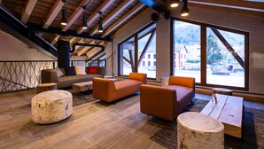 A modern lounge area with wooden flooring, a sofa, ottoman, and a coffee table. Large windows offer a view of the outside. - Chambre Cosy! Parfait pour Travail à Distance | By LeaveTown (Bourg Saint Maurice)