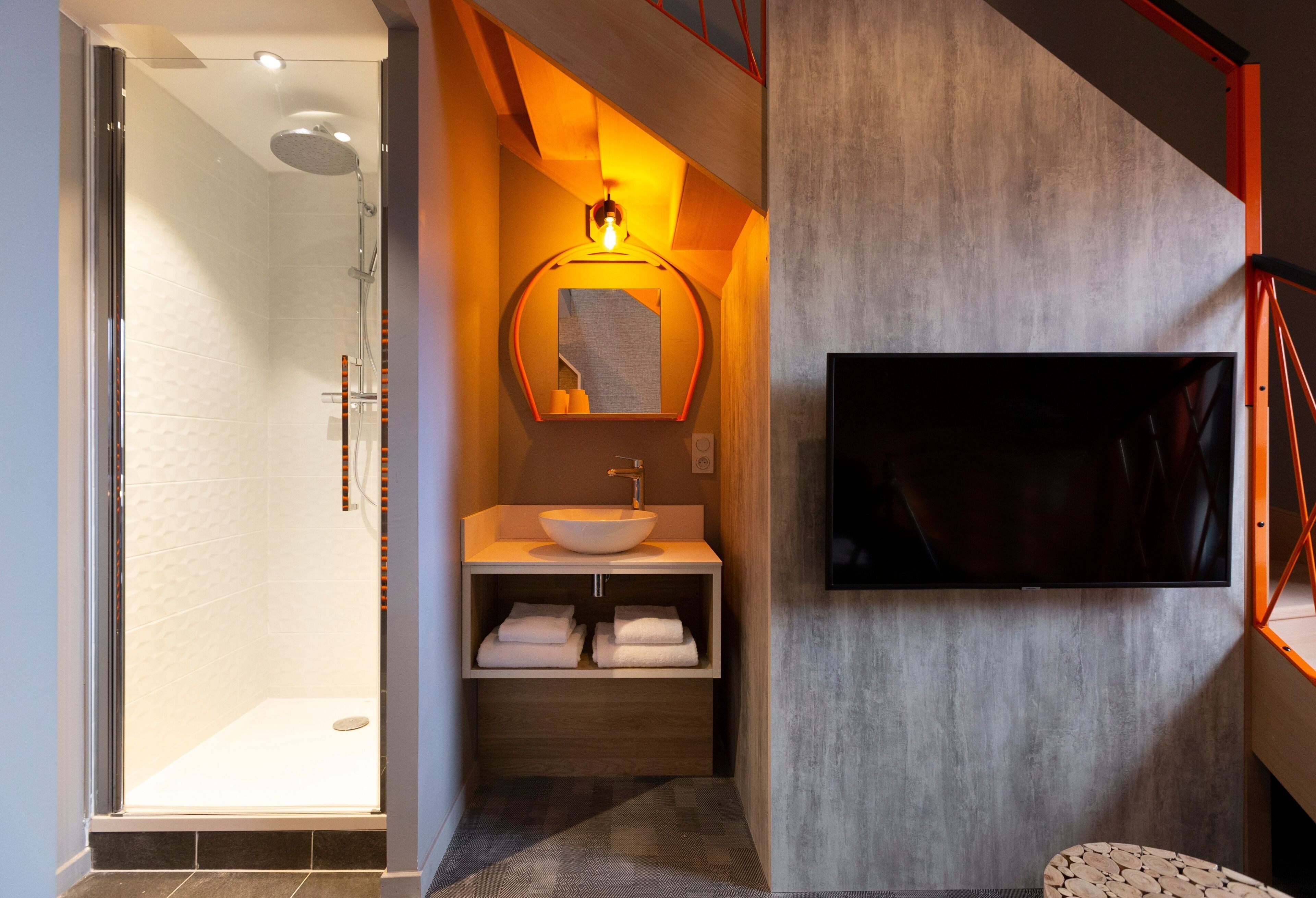 Een moderne badkamer met een glazen douchecabine, een houten wastafelmeubel met een wastafel en een wandtelevisie.