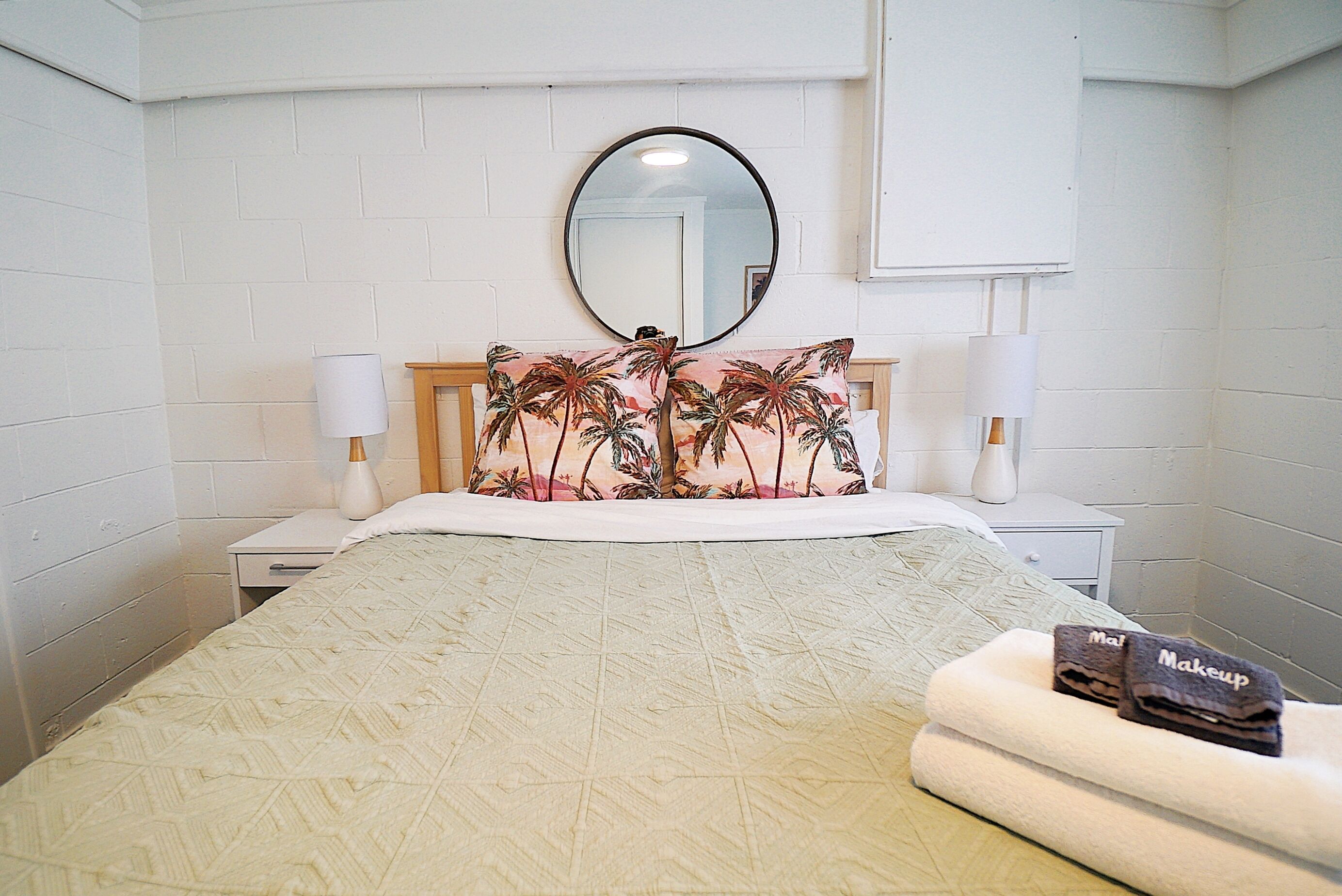 A neatly arranged bedroom with a bed, two bedside tables, a nightstand, a mirror, and a towel rack.