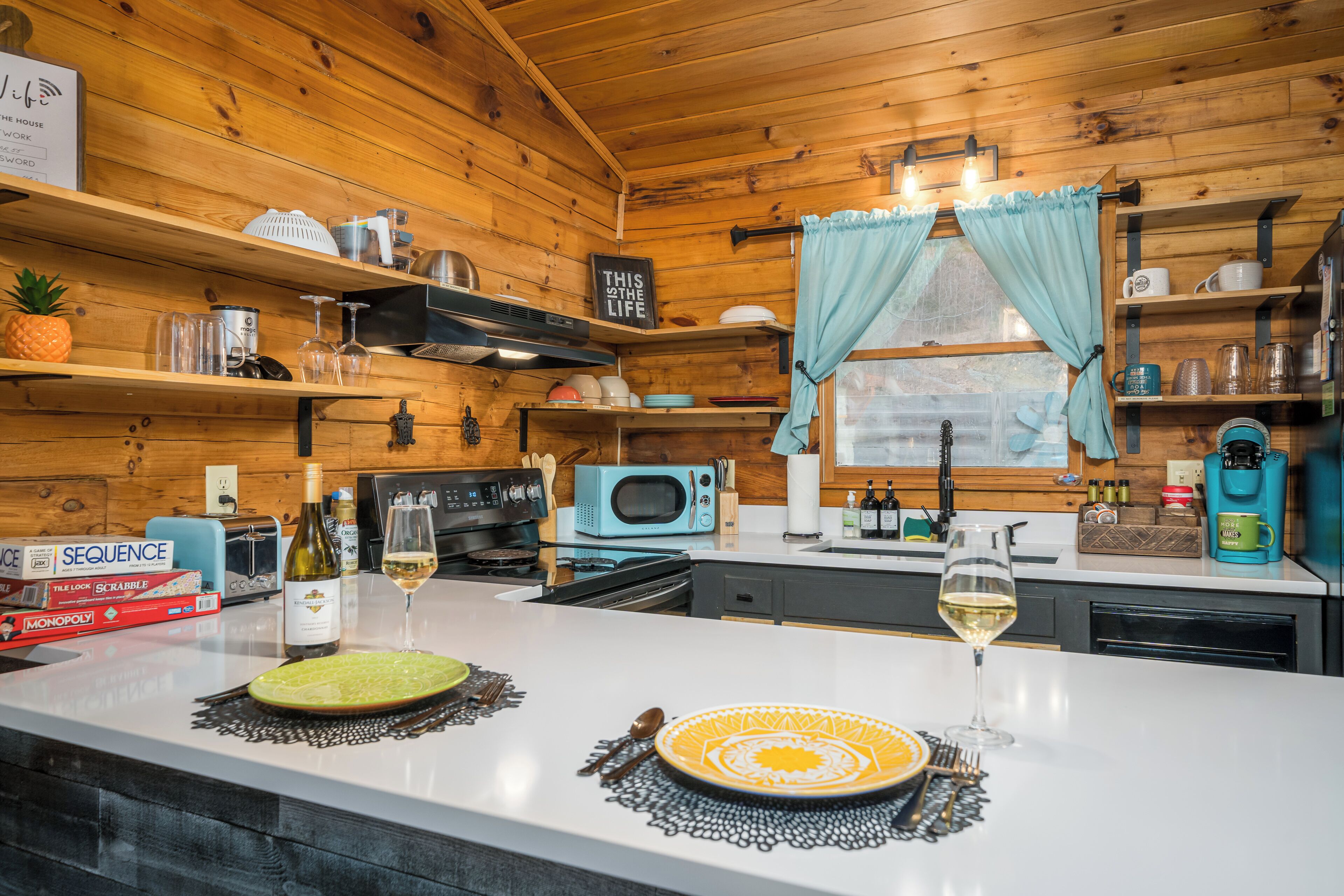 A cozy kitchen with wooden walls, a white countertop, and a window with curtains.