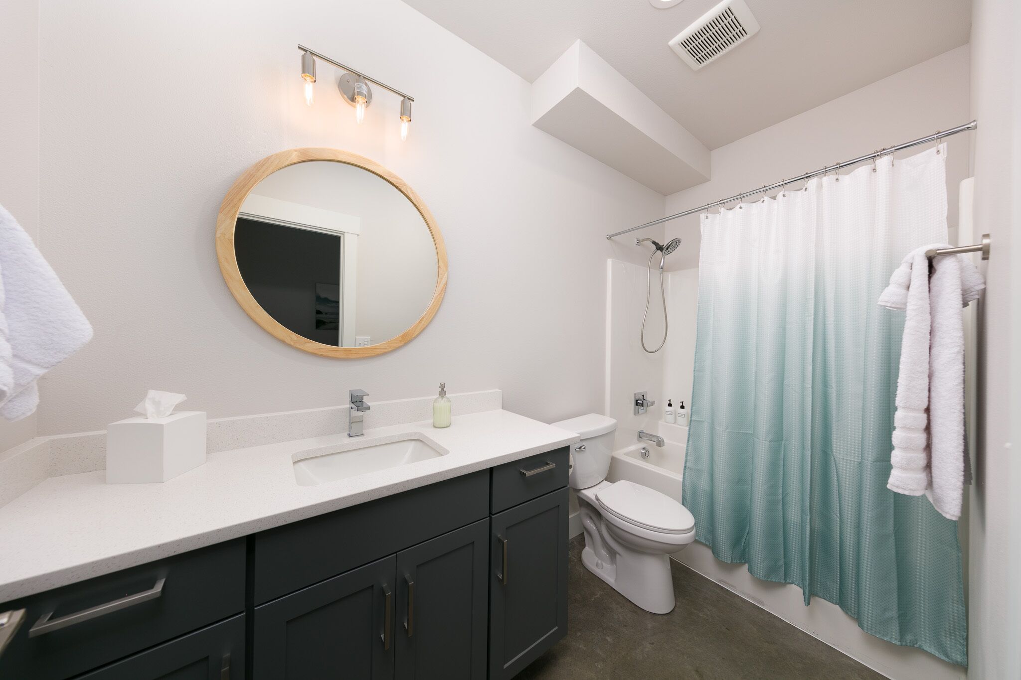 A modern bathroom with a round mirror, white sink, dark cabinets, a toilet, and a shower curtain.