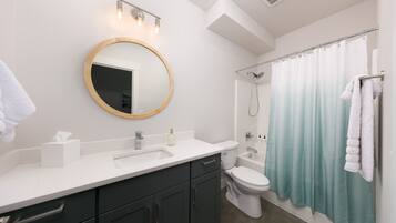 A modern bathroom with a round mirror, white sink, dark cabinets, a toilet, and a shower curtain.