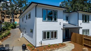 Ein modernes, zweistöckiges Haus mit einer Steinterrasse und einem umzäunten Garten.