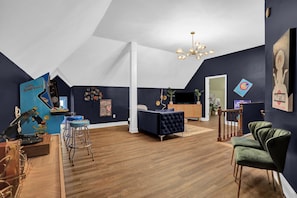 Una sala de estar moderna con una pared de acento azul oscuro, un sofá azul, un sillón azul oscuro, una mesa de centro de madera y una lámpara colgante.