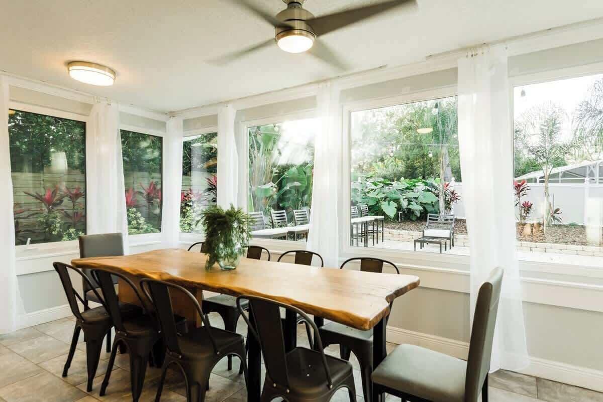 A dining area with a wooden table and chairs, large windows with curtains, and a ceiling fan.