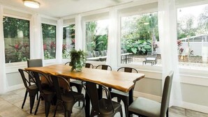 Un comedor con mesa y sillas de madera, ventanas amplias con cortinas y un ventilador de techo.