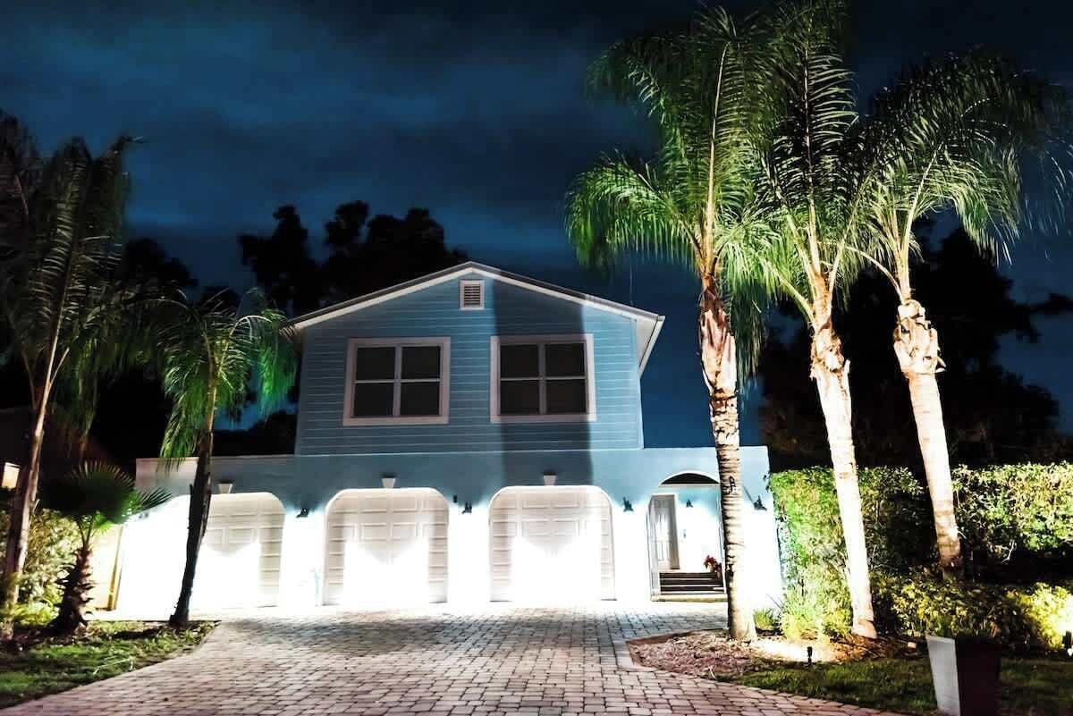 A two-story house with a blue exterior, a driveway, and palm trees.