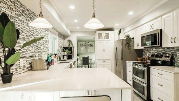 Una cocina moderna con muebles blancos, electrodomésticos de acero inoxidable e iluminación colgante.