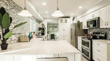 A modern kitchen with white cabinetry, stainless steel appliances, and pendant lighting.