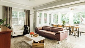 Un salón espacioso con un sofá blanco, un sofá modular de cuero marrón y un comedor con mesa y sillas.