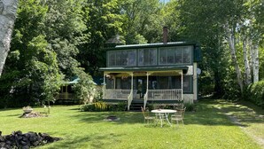 A two-story house with a porch, surrounded by a well-maintained lawn and trees.