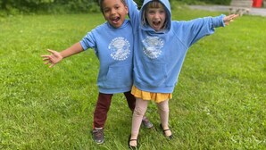 Two children in blue hoodies standing in a grassy area.