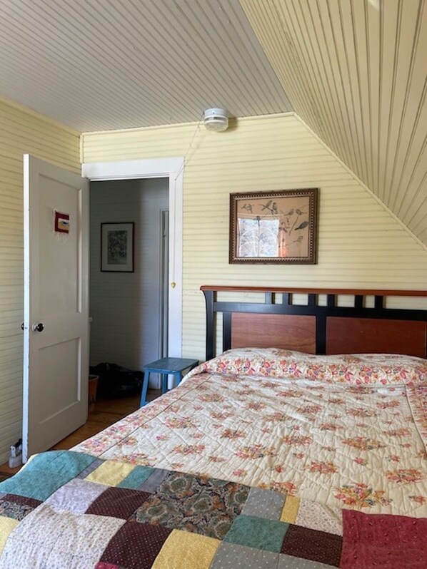 Un dormitorio con una cama de madera, colcha, un cuadro enmarcado en la pared y una puerta que da a otra habitación.