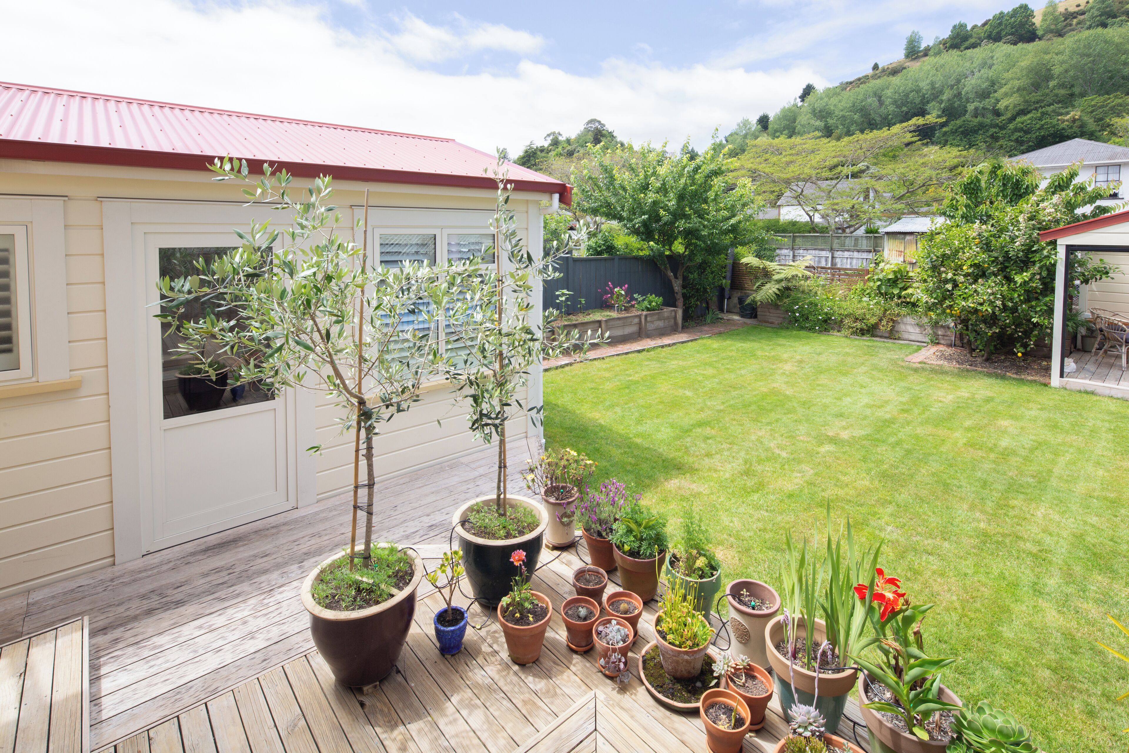 Una terraza de madera con plantas en macetas y una casa con techo rojo.