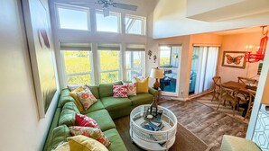 A spacious living room with a green sofa, a coffee table, and a dining area with wooden chairs.