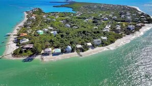 An aerial view of a coastal property with multiple houses, a beach, and clear blue waters.