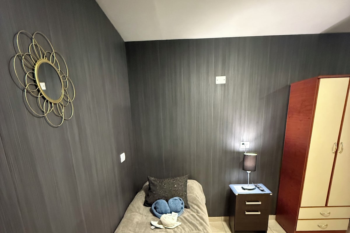 Une chambre à coucher comprenant un lit, une table de chevet, une lampe, une armoire et un élément de décoration murale.