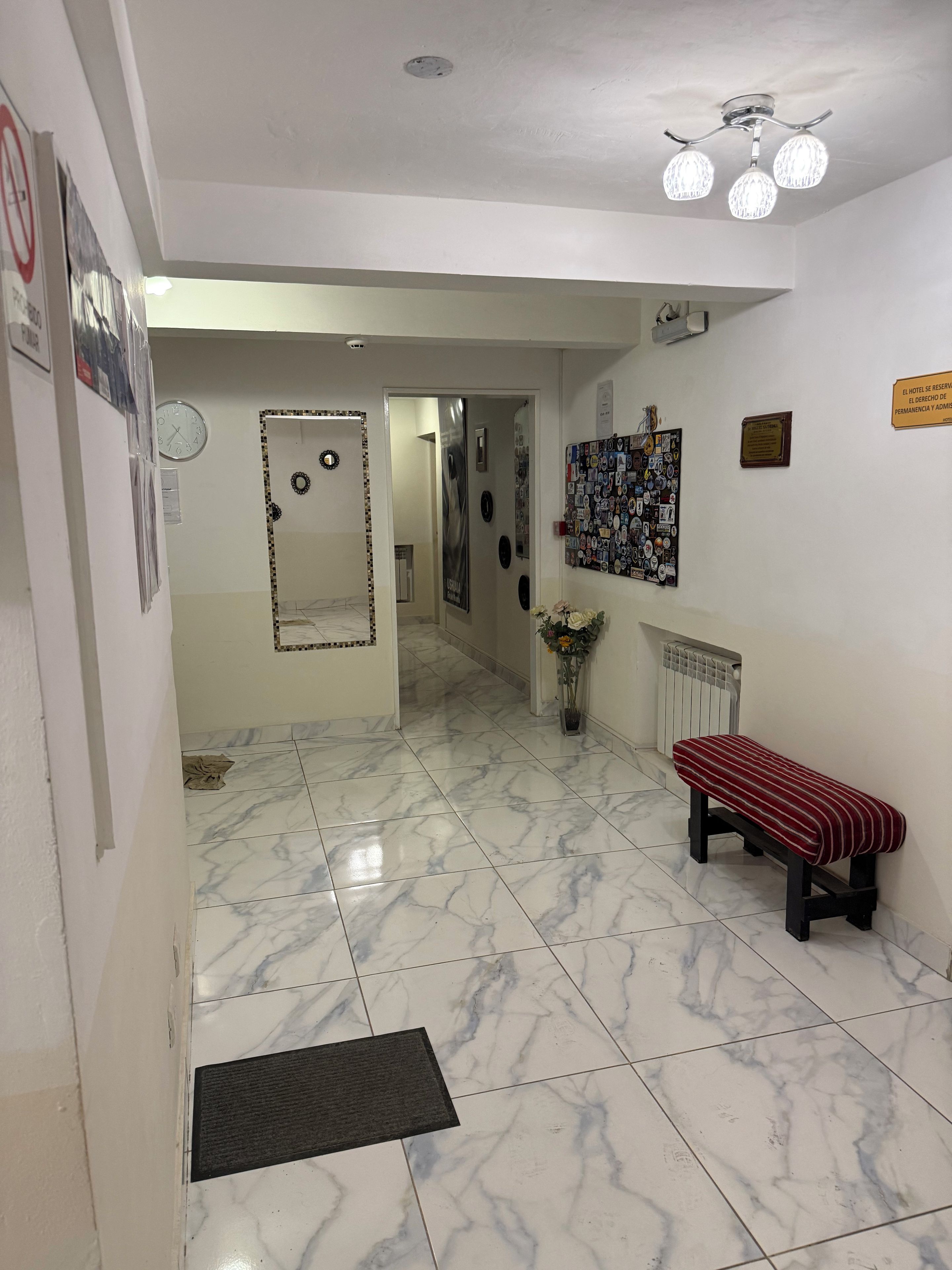 Un pasillo de hotel con un banco, un reloj de pared, un tablón de anuncios y un radiador.