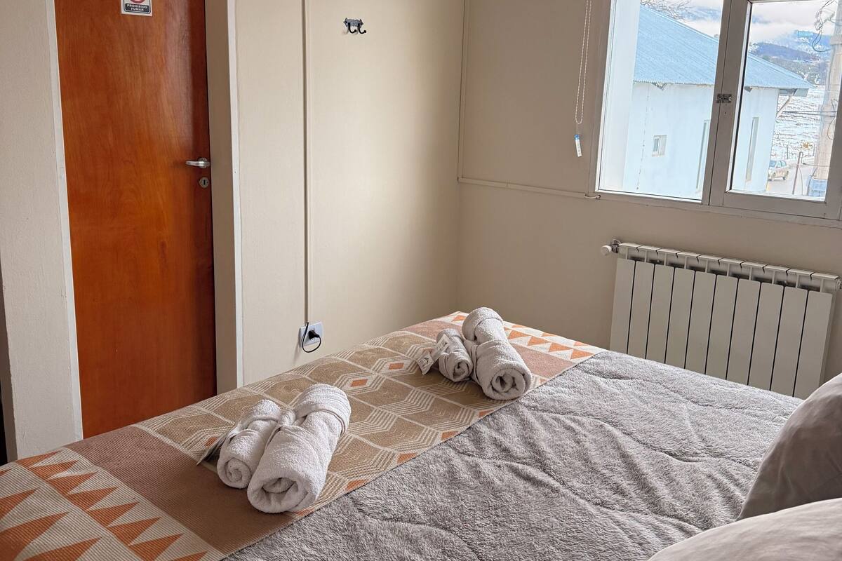 Une chambre d’hôtel avec un lit, un téléviseur fixé au mur, une fenêtre donnant sur des immeubles et une porte sur laquelle est apposé un panneau « interdiction de fumer ».