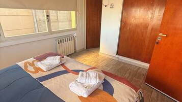 A bedroom with a bed, a TV mounted on the wall, and a window with blinds.