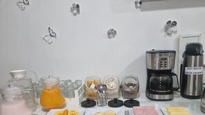 Un bufé de desayuno con diversas opciones de comida y bebidas, incluyendo gajos de naranja, rebanadas de manzana y agua caliente.