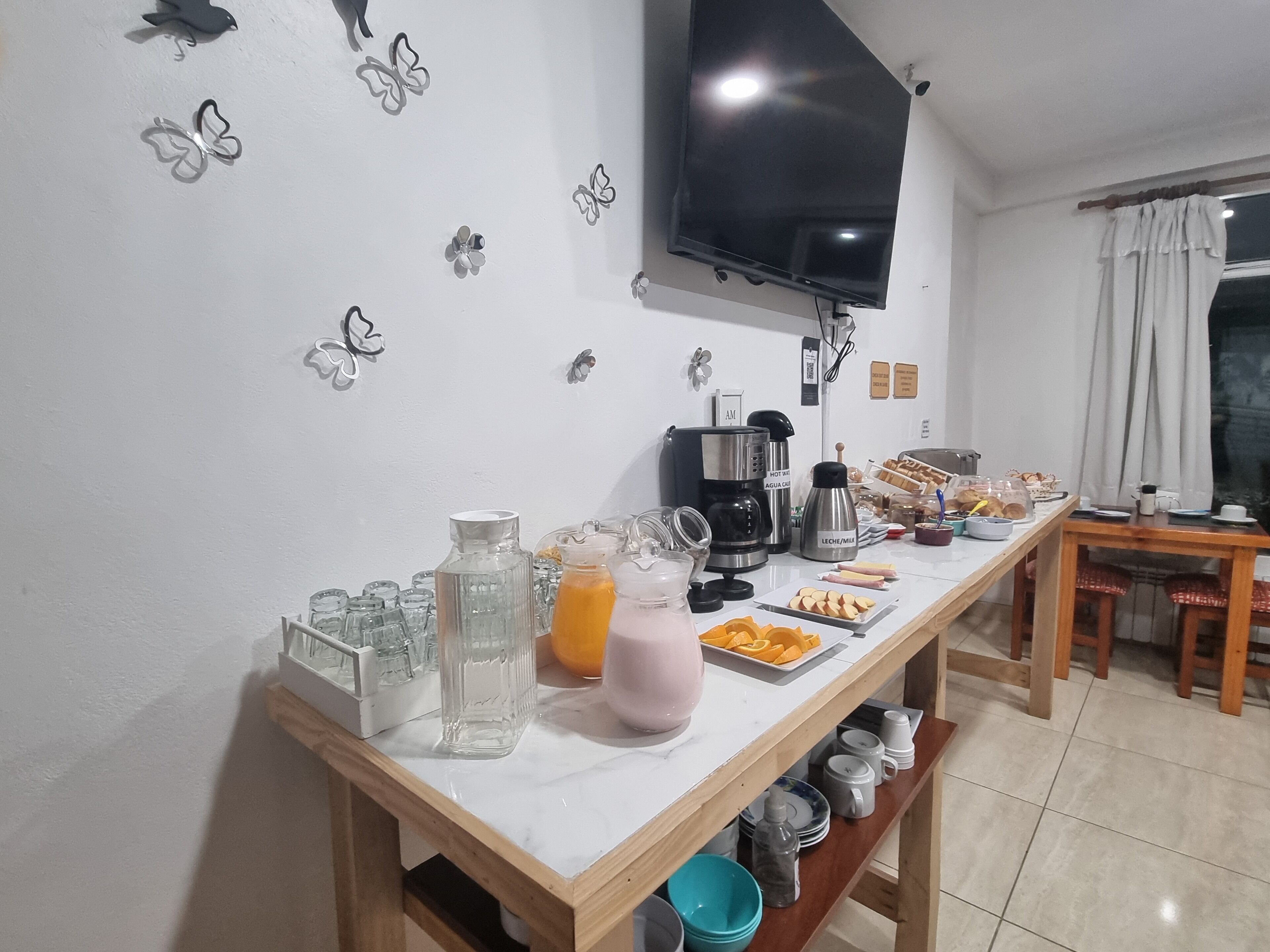 Montaje de un bufé de desayuno con una cafetera, un jarro de jugo y diferentes alimentos sobre una mesa.