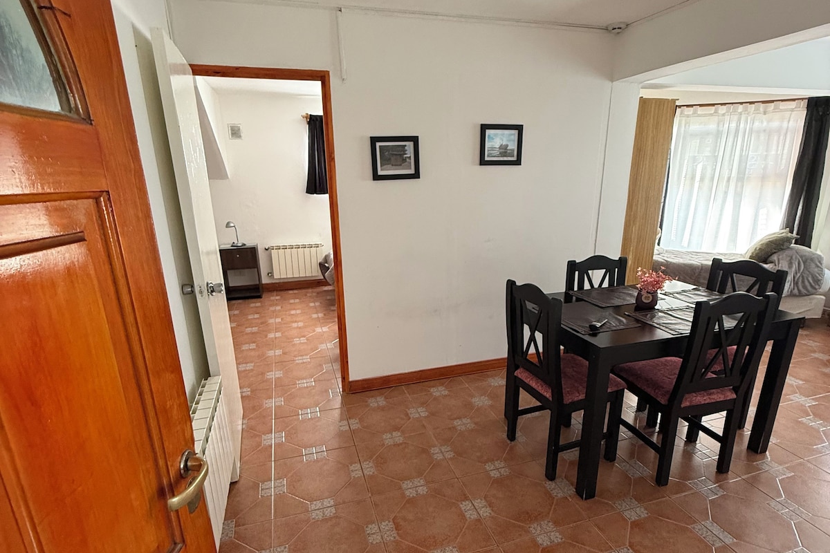 Un coin repas avec une table et des chaises, un ventilateur de plafond et une vue sur l’extérieur grâce à une porte ouverte.