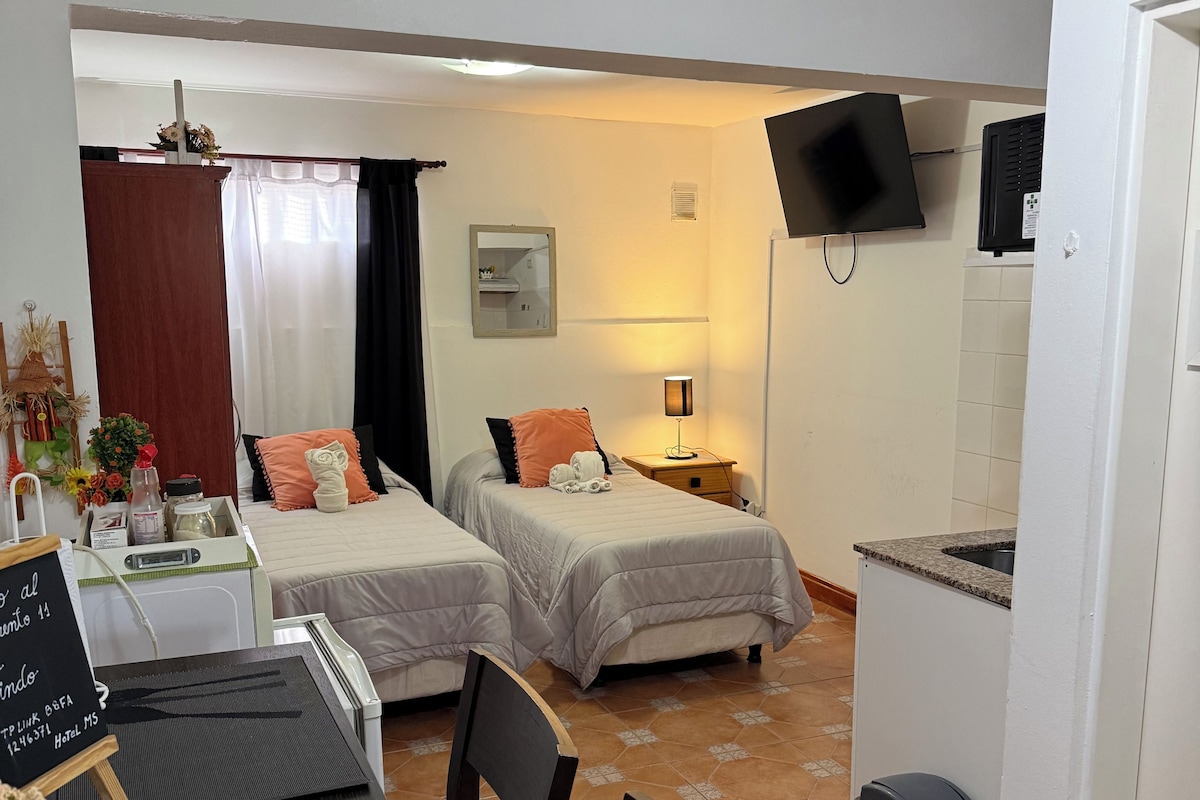 Une chambre d’hôtel avec deux lits, une table à manger, des chaises, un téléviseur et un petit coin cuisine.