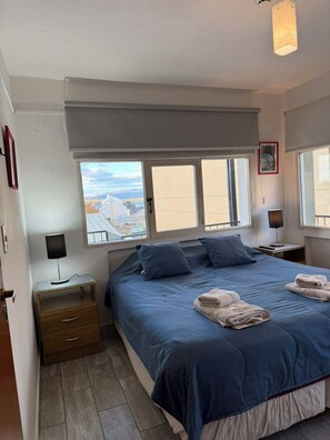 Un dormitorio con cama, dos mesitas de noche, una ventana con vistas y una lámpara en el techo.