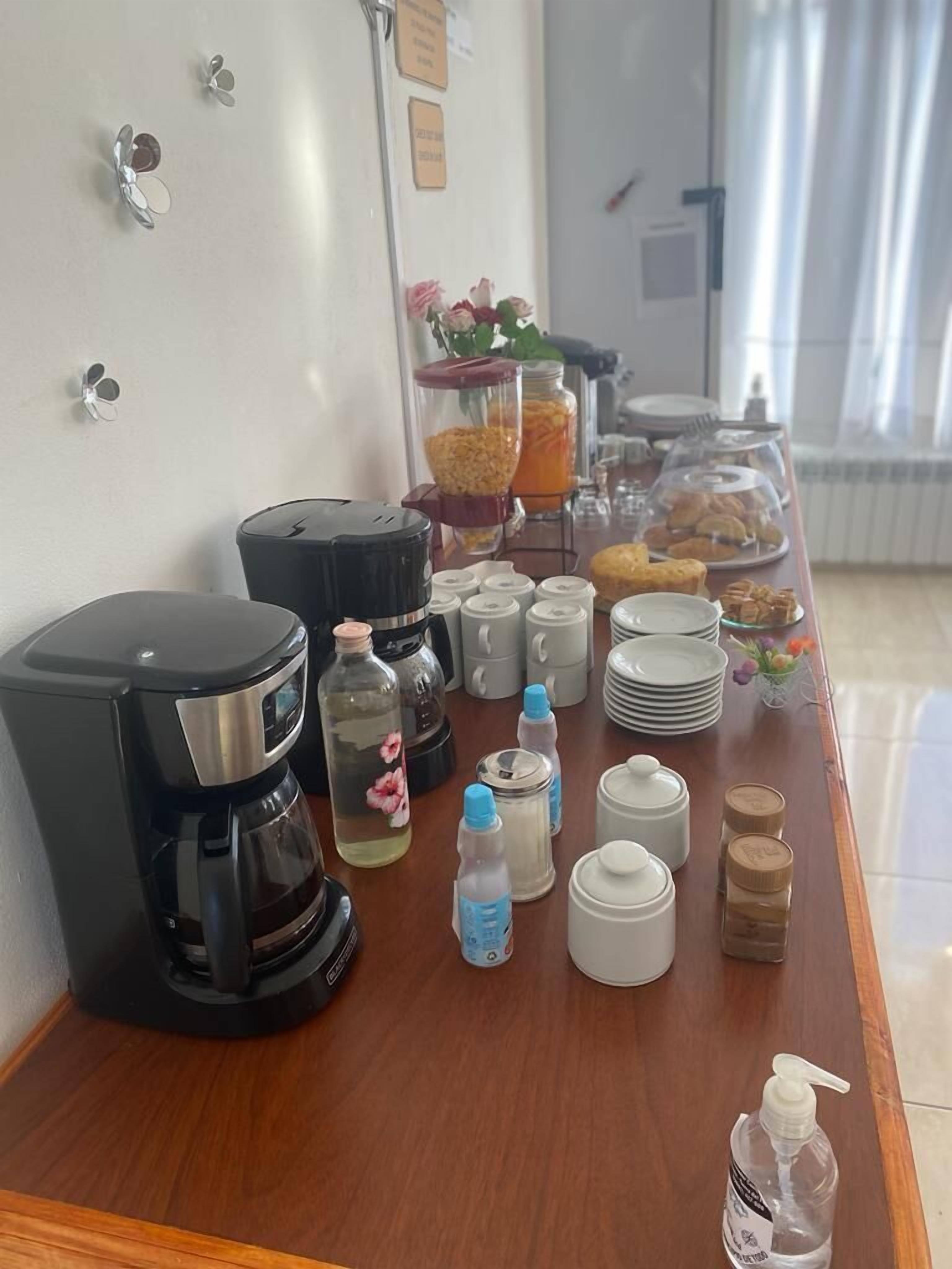 A breakfast buffet setup with a coffee maker, water bottles, condiment dispensers, and a variety of pastries and fruits.