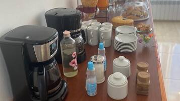 A breakfast buffet setup with a coffee maker, water bottles, condiment dispensers, and a variety of pastries and fruits.