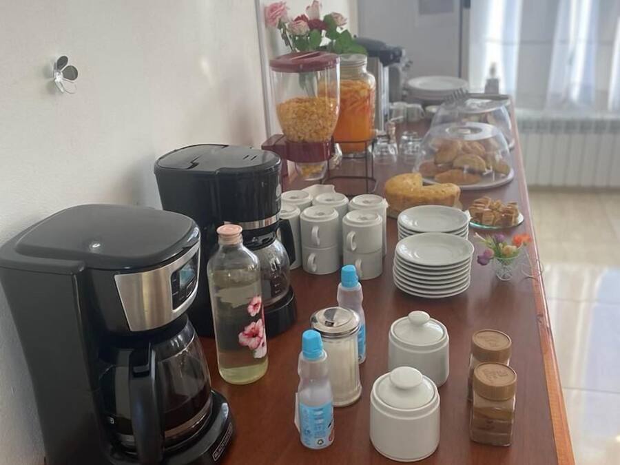 A breakfast buffet setup with a coffee maker, water bottles, condiment dispensers, and a variety of pastries and fruits.