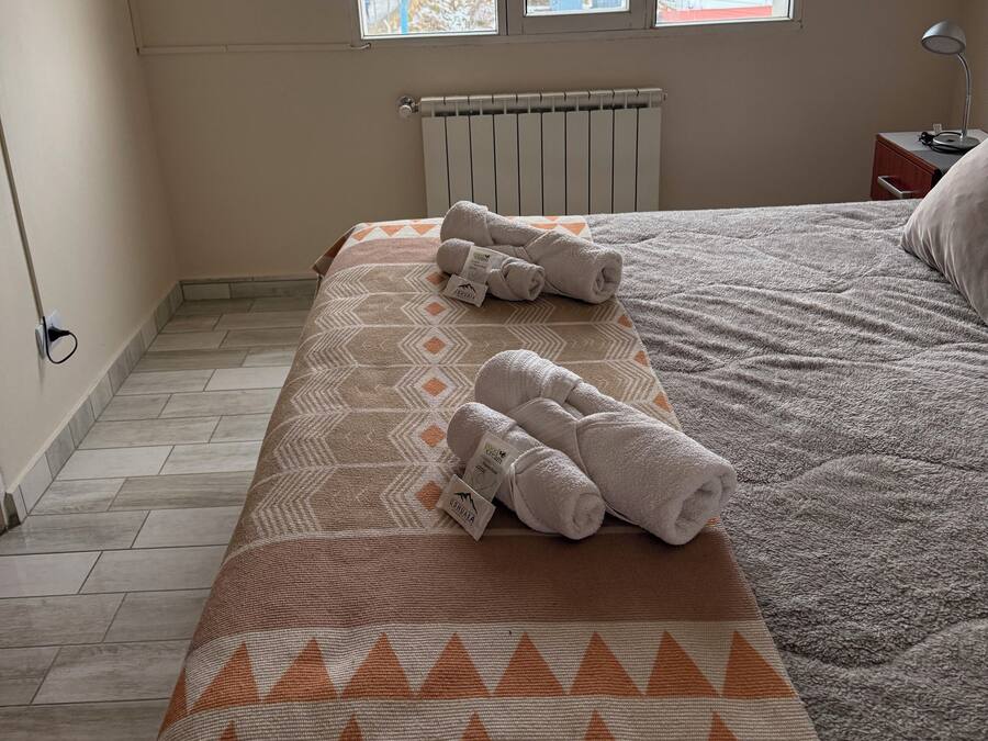 A bedroom with a bed, a window with a view of a snowy landscape, a radiator, and a bedside table with a lamp.